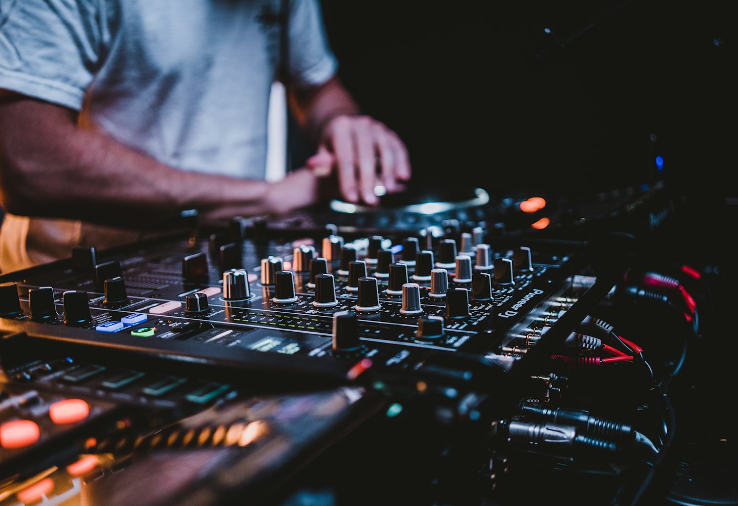DJ's hands adjusting controls on a mixing console and turntable.